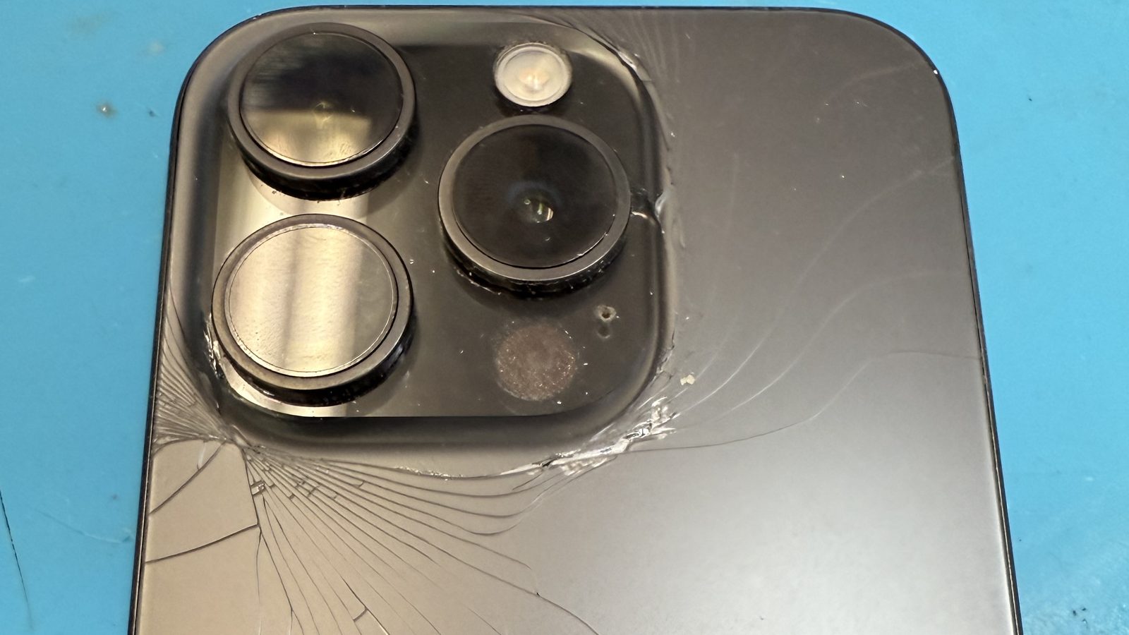 Cracked iPhone back glass radiating from the camera housing