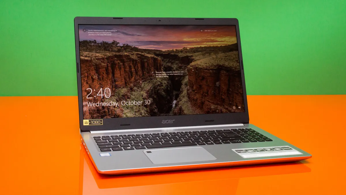 A silver Acer laptop with a 1080p screen displays a scenic landscape background, showing the time as 2:40 on an orange table.