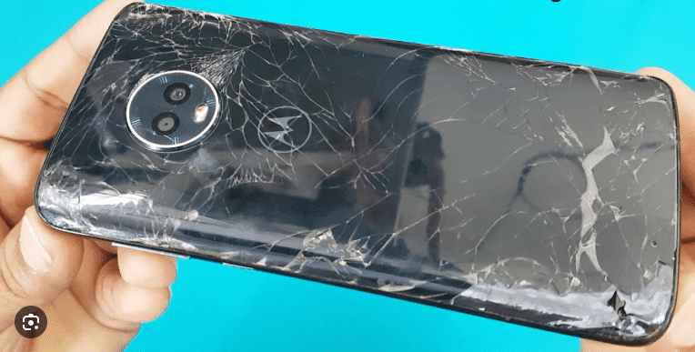 a hand holding a motorola moto x4 with a cracked screen, emphasizing the extent of the damage to the smartphone